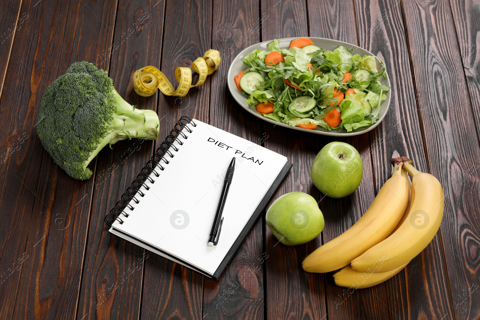 Photo of Notebook with phrase Diet Plan, measuring tape and different products on wooden table. Weight loss concept