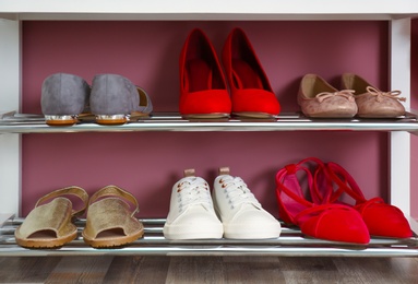 Photo of Collection of stylish shoes on rack storage near color wall