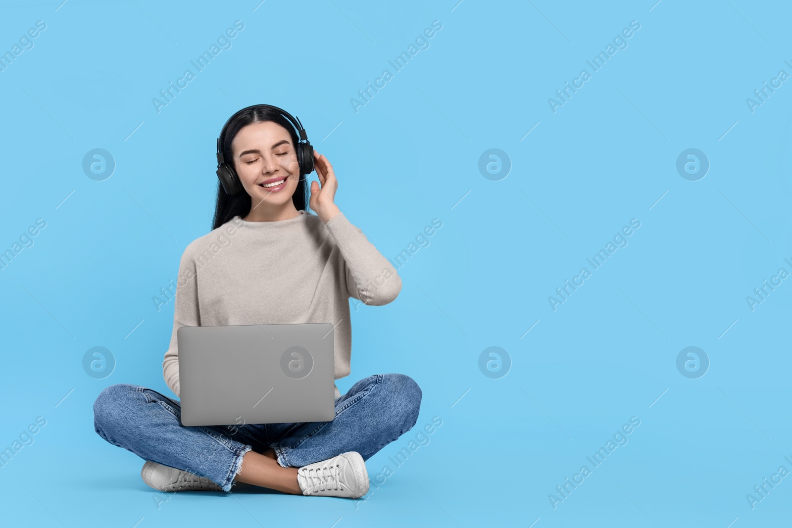 Photo of Happy woman with laptop listening to music in headphones on light blue background, space for text