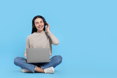 Photo of Happy woman with laptop listening to music in headphones on light blue background, space for text