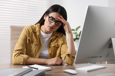 Photo of Young woman suffering from headache at wooden table in office