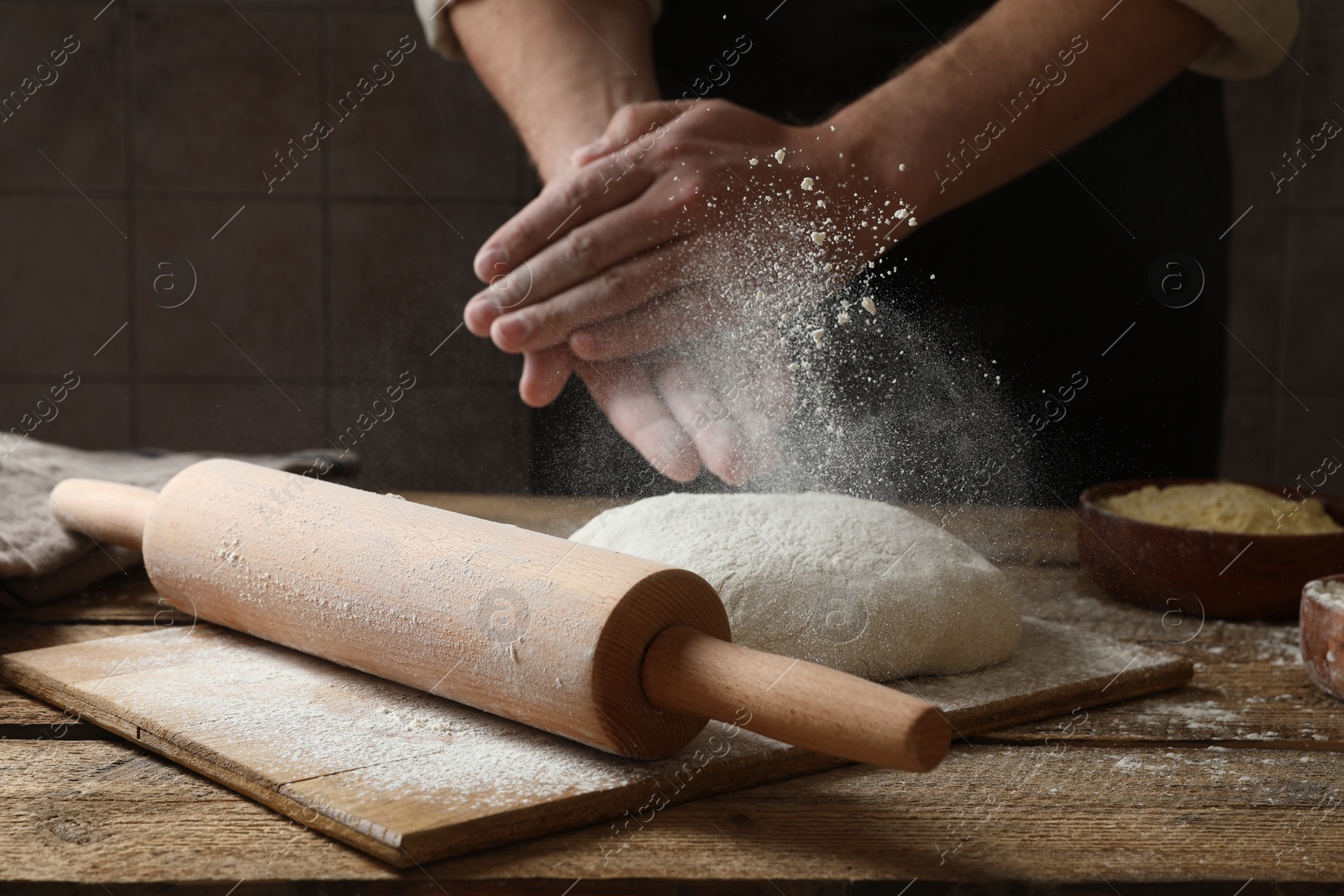 Photo of Man sprinkling flour over dough at wooden table, closeup