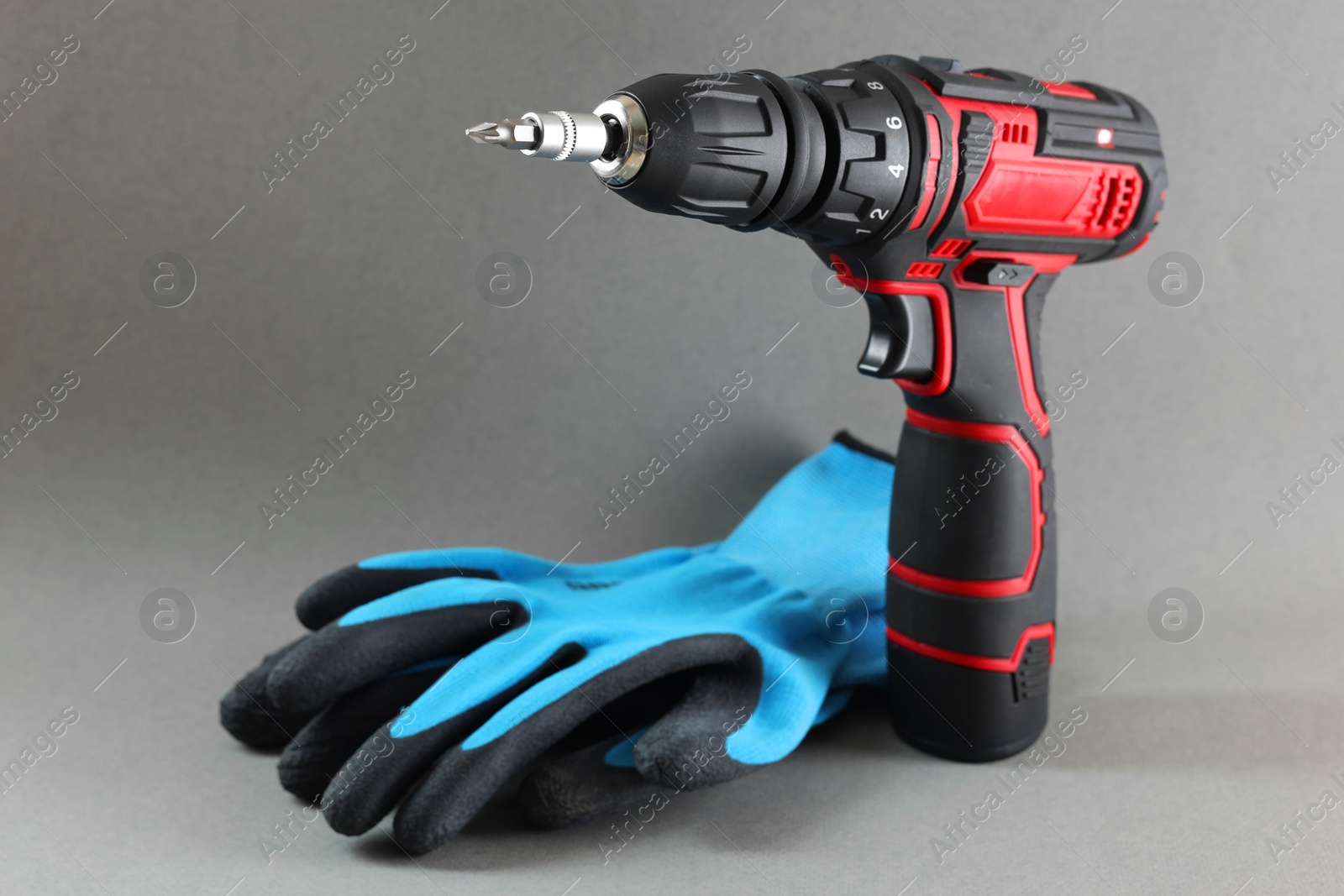 Photo of Modern electric screwdriver and gloves on grey background