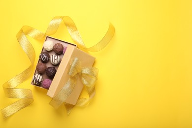 Photo of Open box with delicious chocolate candies and ribbon on yellow background, top view. Space for text