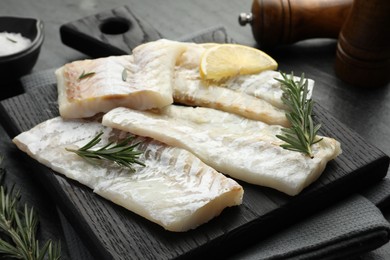 Photo of Fresh raw cod fillets with rosemary and lemon on table, closeup