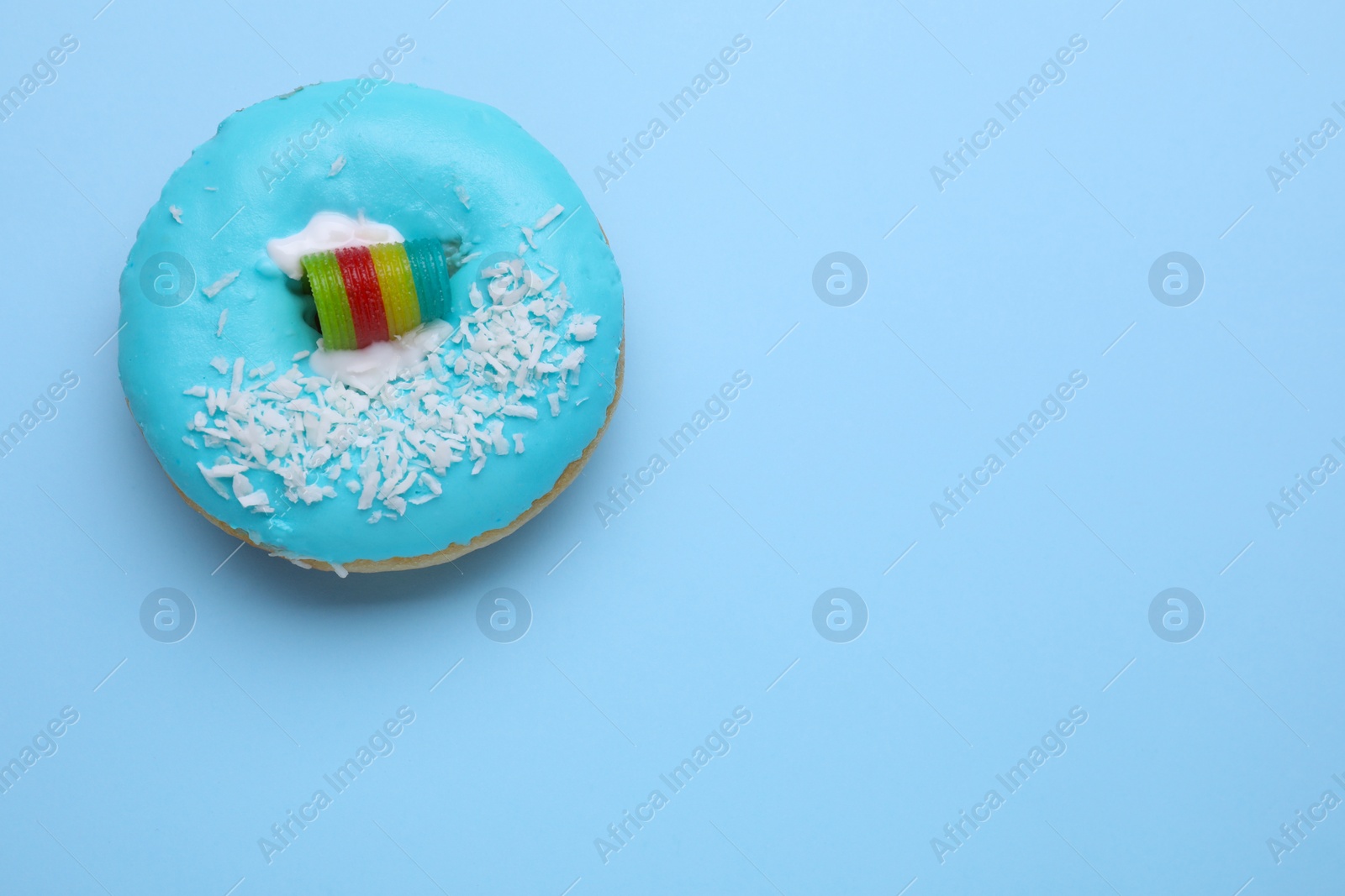 Photo of Tasty glazed donut decorated with coconut shavings and rainbow sour candy on light blue background, top view. Space for text