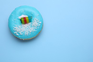 Tasty glazed donut decorated with coconut shavings and rainbow sour candy on light blue background, top view. Space for text