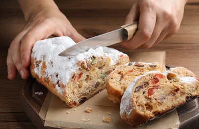 Photo of Woman cutting traditional Christmas Stollen at wooden table, closeup