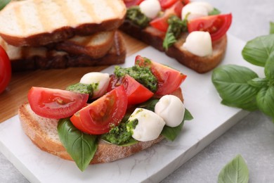 Photo of Delicious Caprese sandwiches with mozzarella, tomatoes, basil and pesto sauce on light grey table, closeup