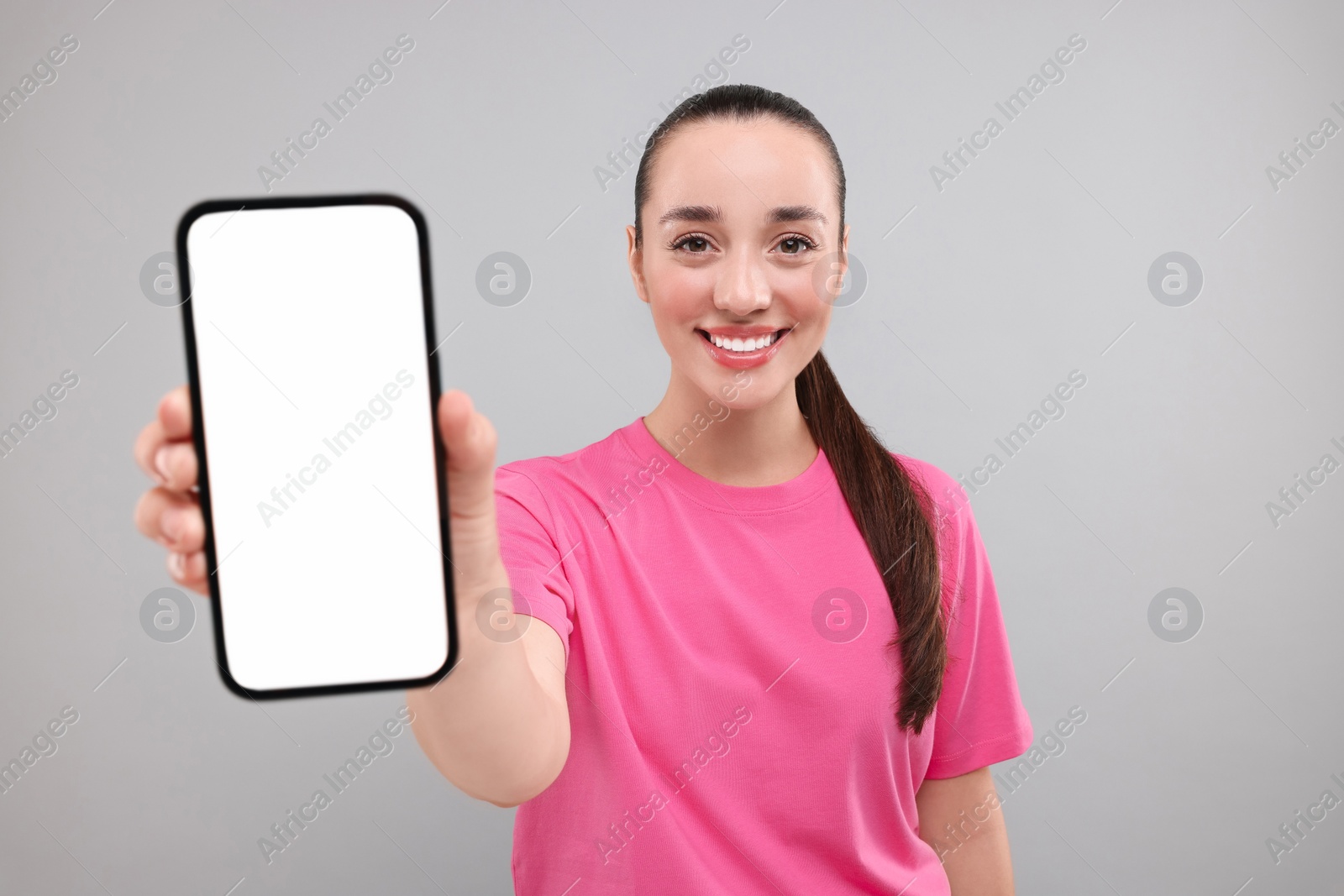 Photo of Young woman showing smartphone in hand on light grey background