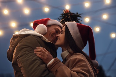 Happy couple kissing under mistletoe bunch outdoors, low angle view