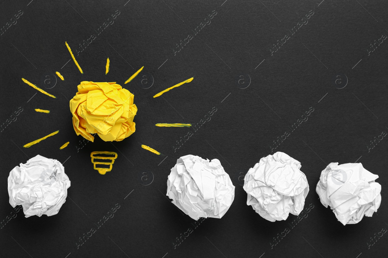 Photo of Flat lay composition with yellow crumpled paper ball and drawing of lamp bulb on blackboard. Idea concept