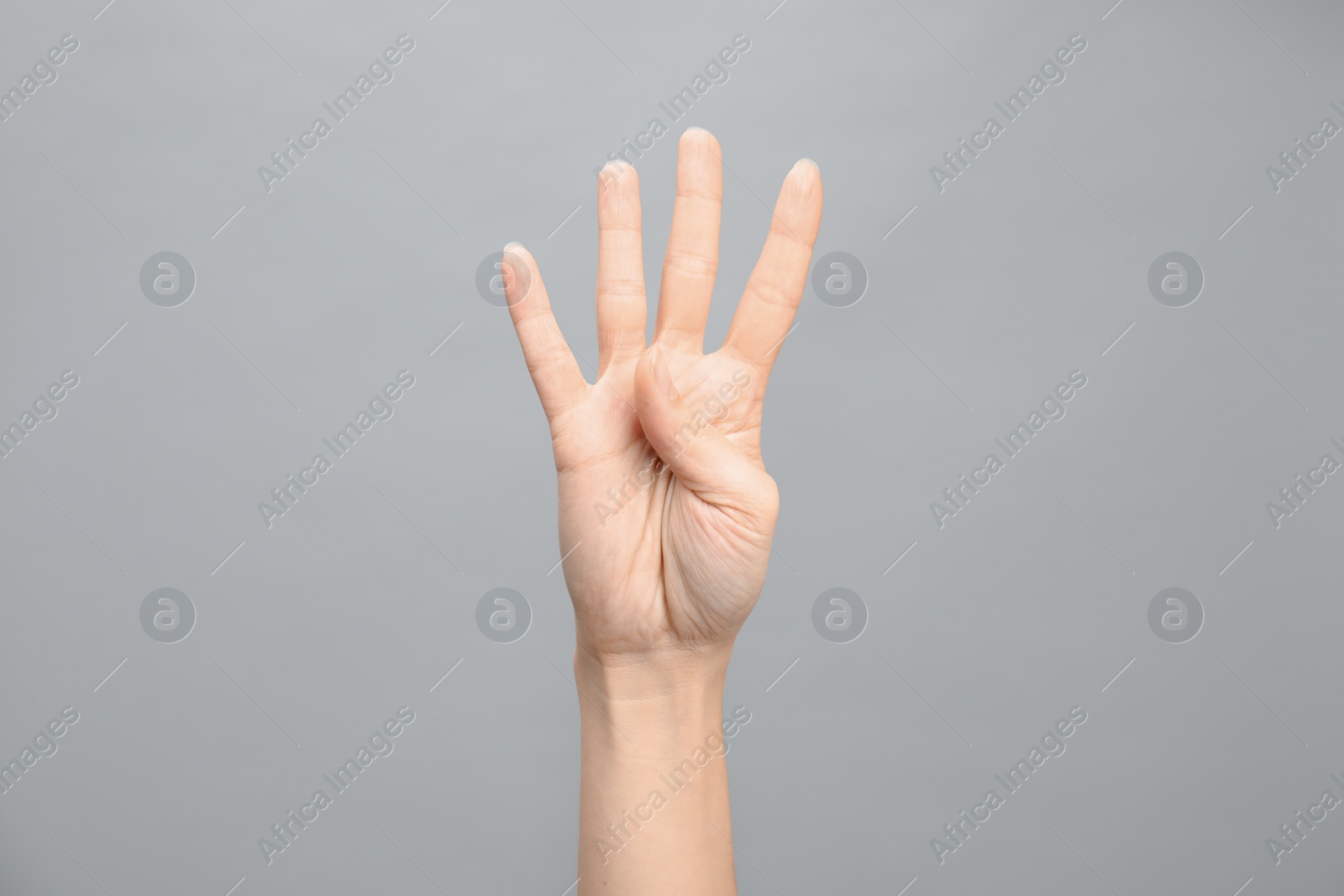 Photo of Woman showing number four on grey background, closeup. Sign language