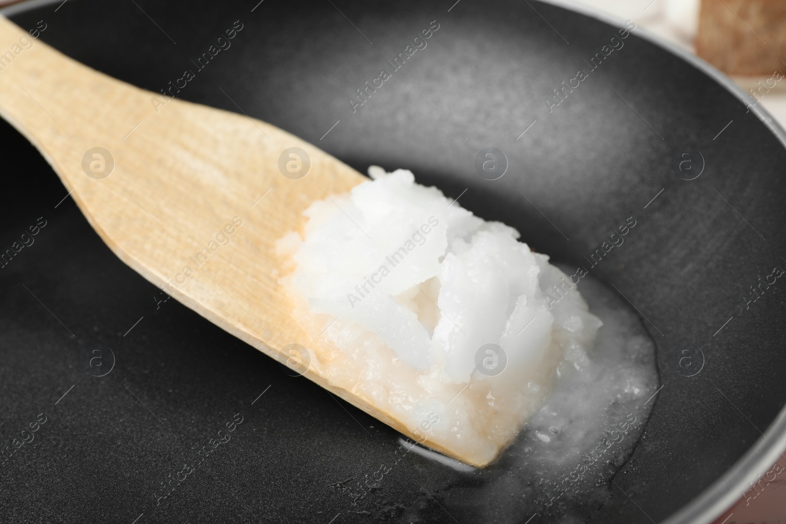 Photo of Frying pan with coconut oil and wooden spatula, closeup. Healthy cooking