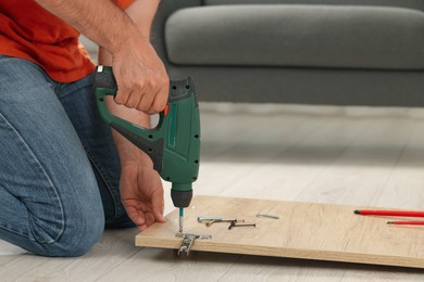 Photo of Man with electric screwdriver assembling furniture on floor indoors, closeup. Space for text