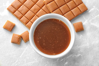 Delicious caramel candies and sauce on light background