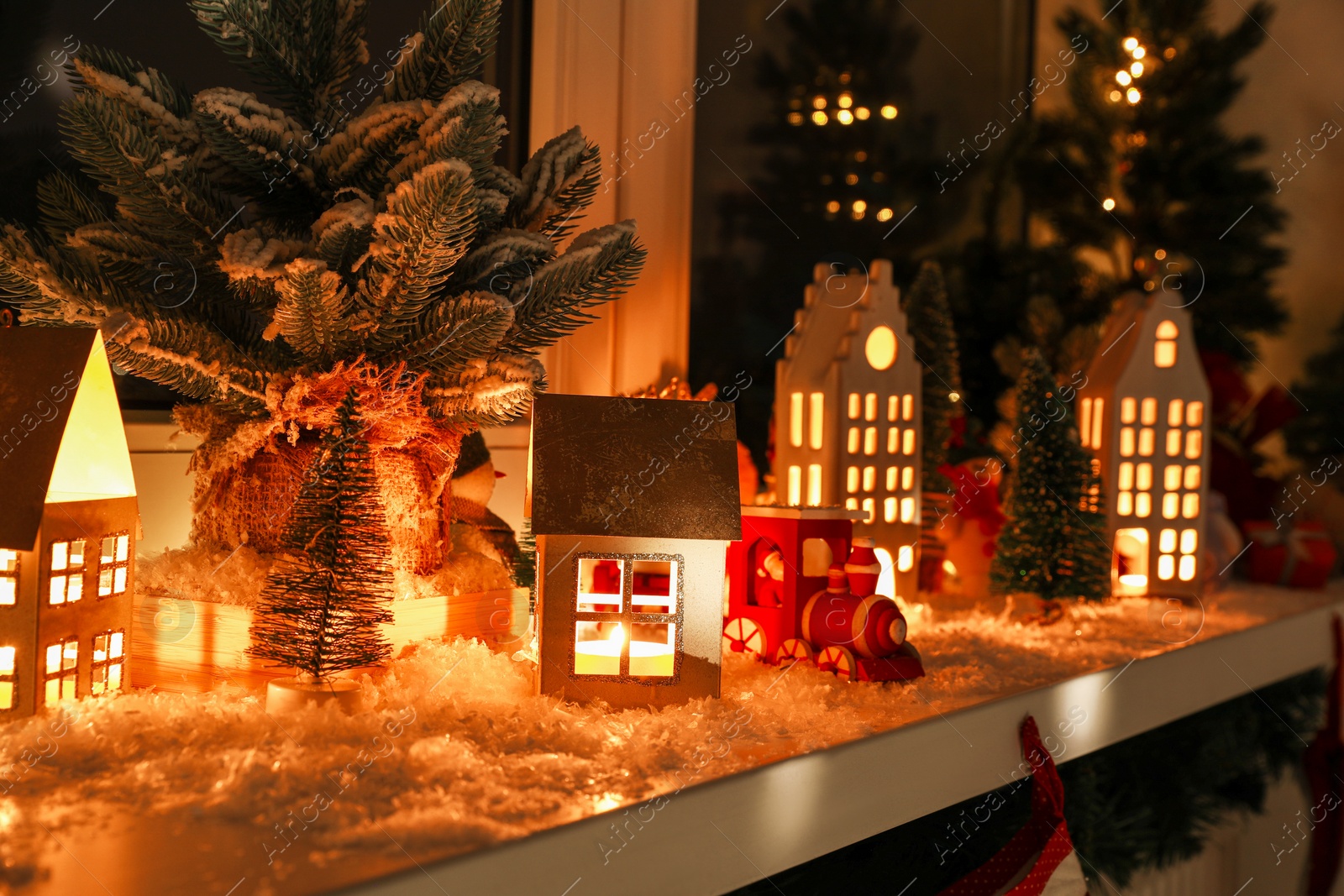 Photo of Christmas atmosphere. Many beautiful glowing houses on window sill indoors