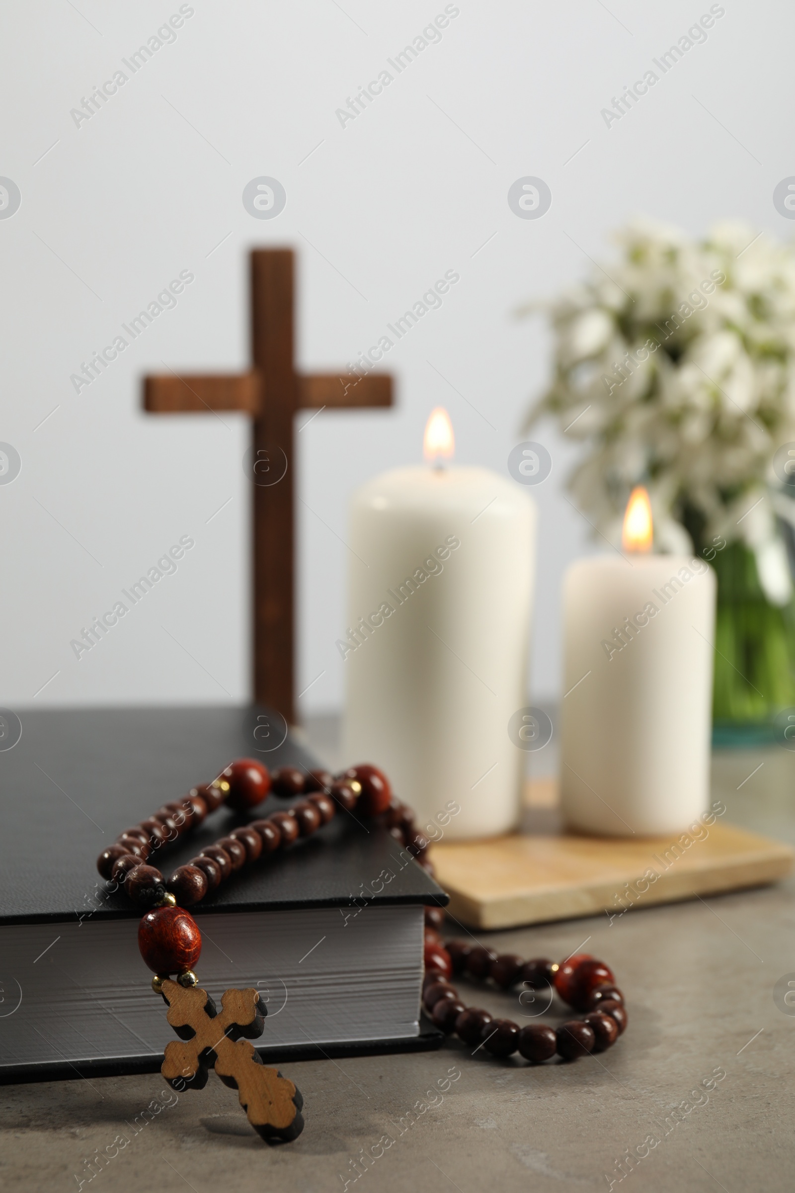 Photo of Bible, rosary beads, wooden cross and church candles on grey table