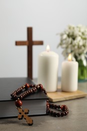 Bible, rosary beads, wooden cross and church candles on grey table