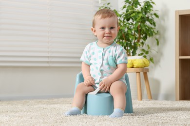 Photo of Little child sitting on plastic baby potty indoors. Space for text