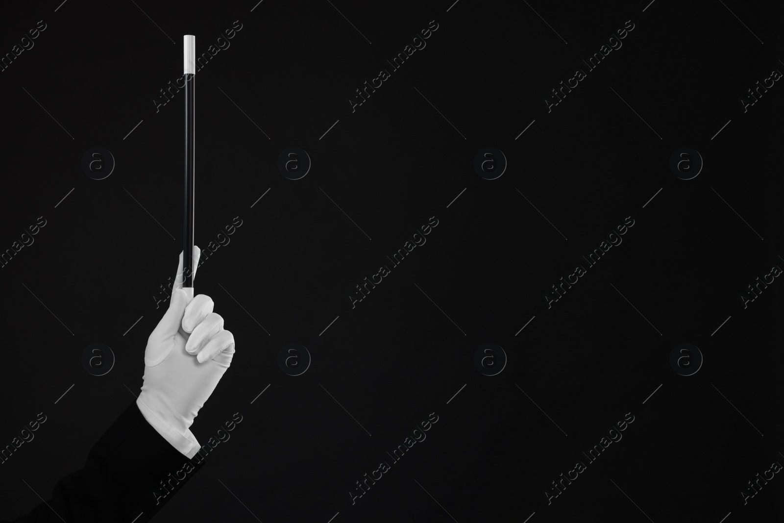 Photo of Magician holding wand on black background, closeup. Space for text