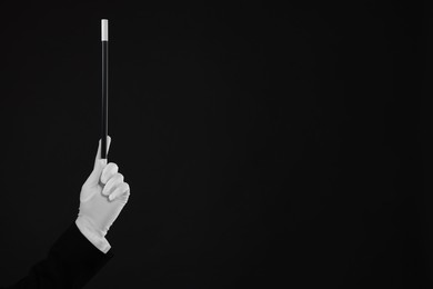 Photo of Magician holding wand on black background, closeup. Space for text