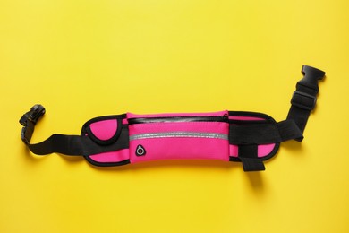 Photo of Stylish pink waist bag on yellow background, top view