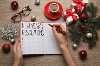 Woman filling list of New Year's resolutions in notebook on wooden table, top view