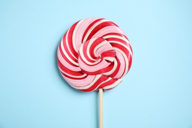 Photo of Stick with colorful lollipop swirl on light blue background, top view