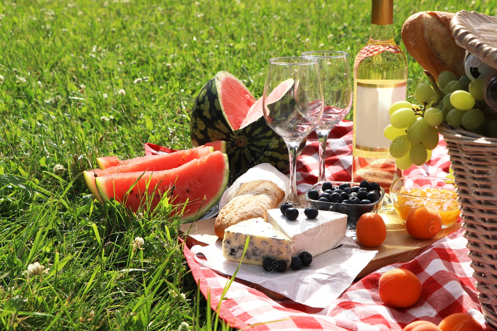 Photo of Picnic blanket with delicious food and wine outdoors on summer day