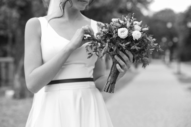 Woman in wedding gown with beautiful bridal bouquet outdoors, black and white effect