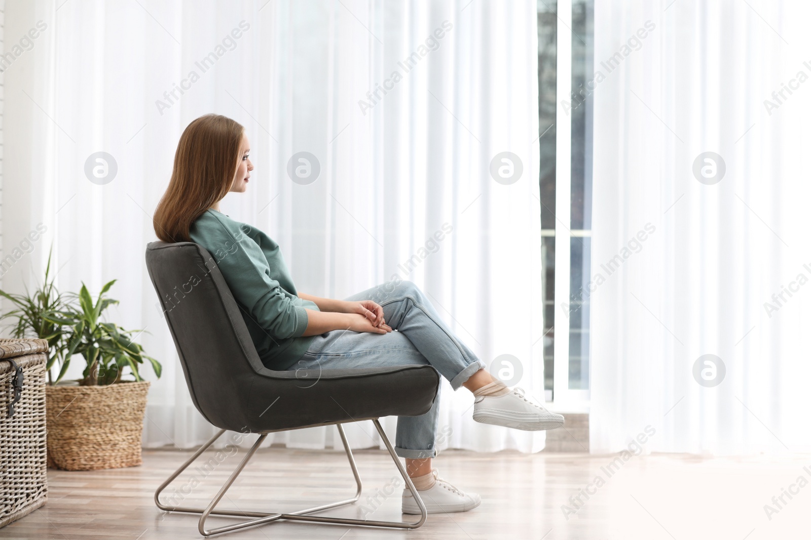 Photo of Young woman sitting in armchair near window at home