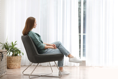 Young woman sitting in armchair near window at home