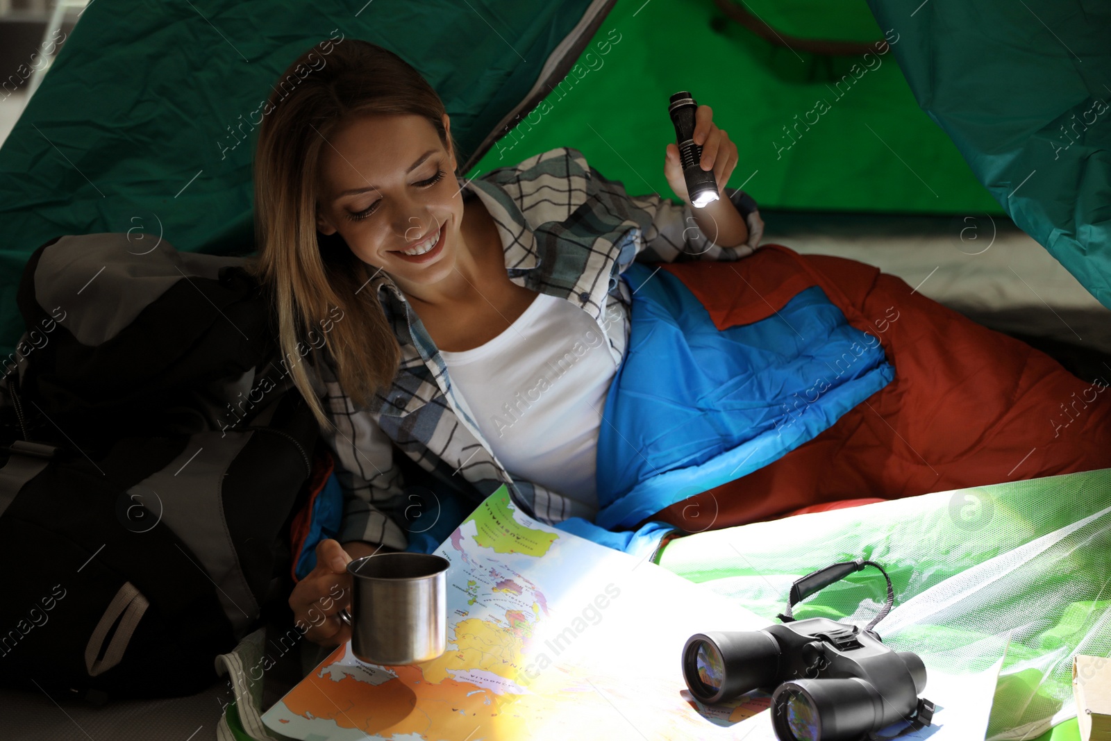Photo of Young woman in sleeping bag with map and flashlight inside of tent