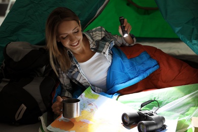 Young woman in sleeping bag with map and flashlight inside of tent