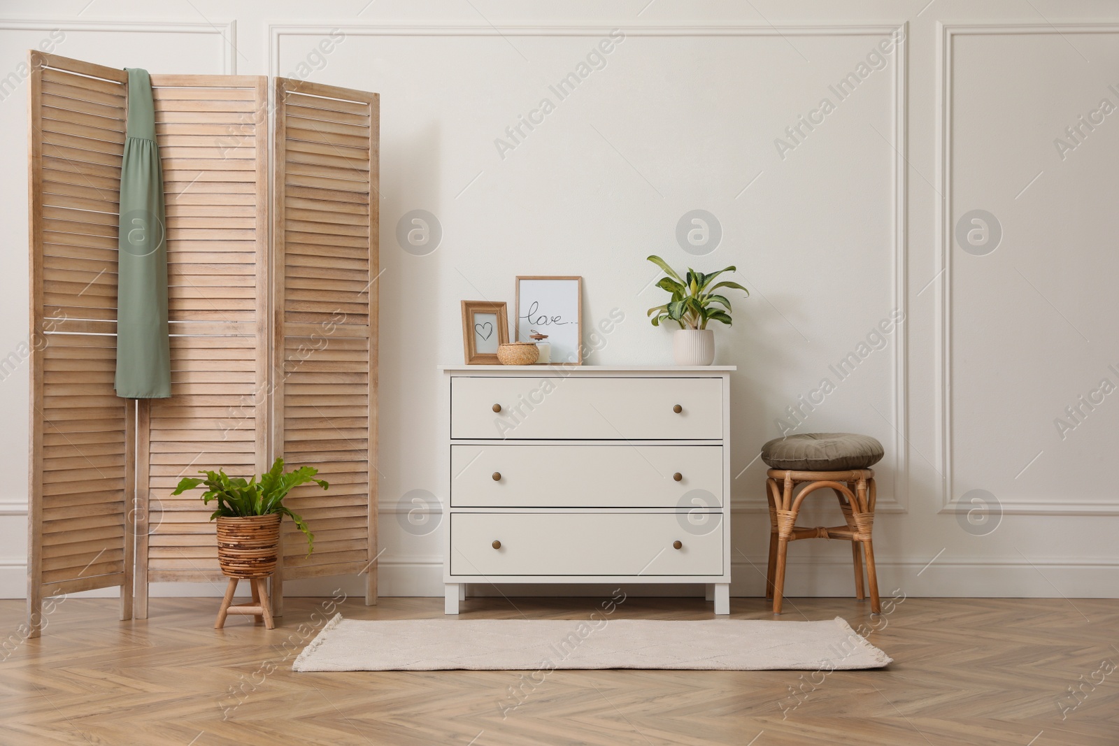 Photo of Stylish room with wooden folding screen and chest of drawers near white wall. Interior design