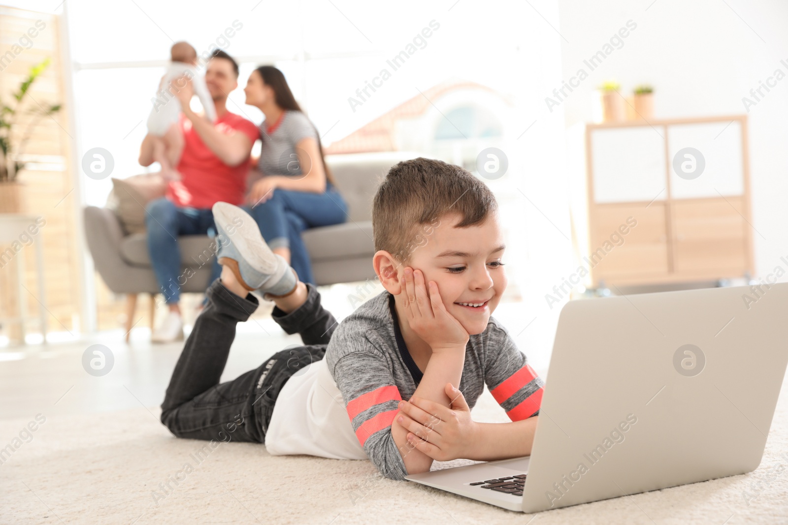 Photo of Boy with laptop lying on carpet near his family at home