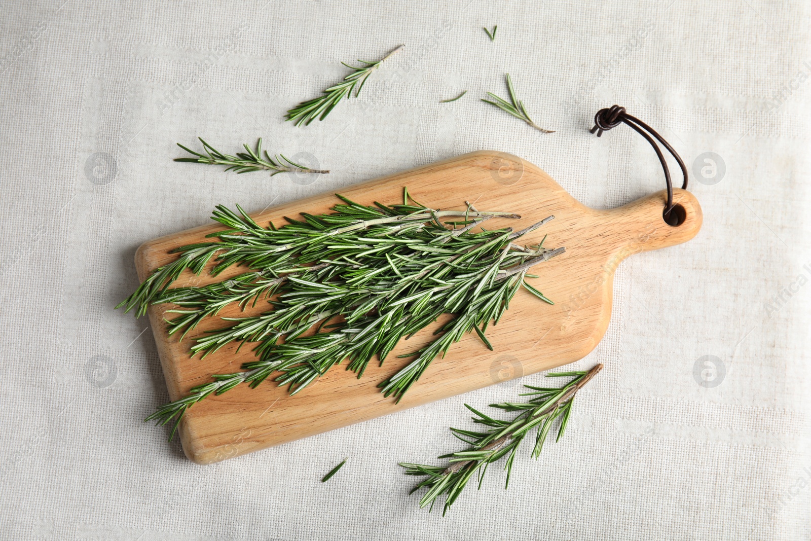 Photo of Wooden board with fresh rosemary twigs on fabric, top view