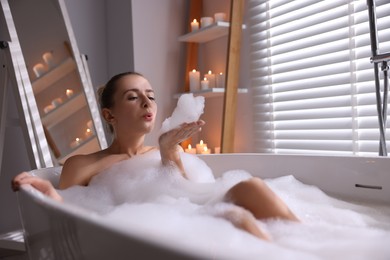Photo of Beautiful woman taking bath in tub with foam indoors