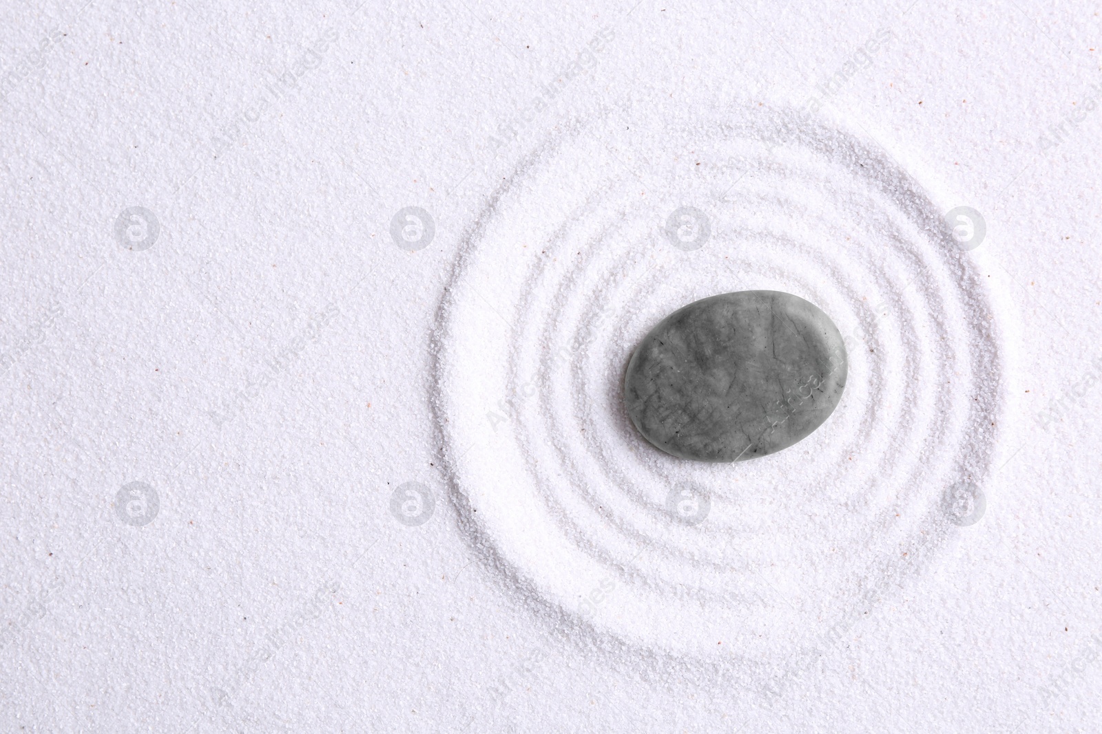 Photo of Zen garden stone on white sand with pattern, top view. Space for text