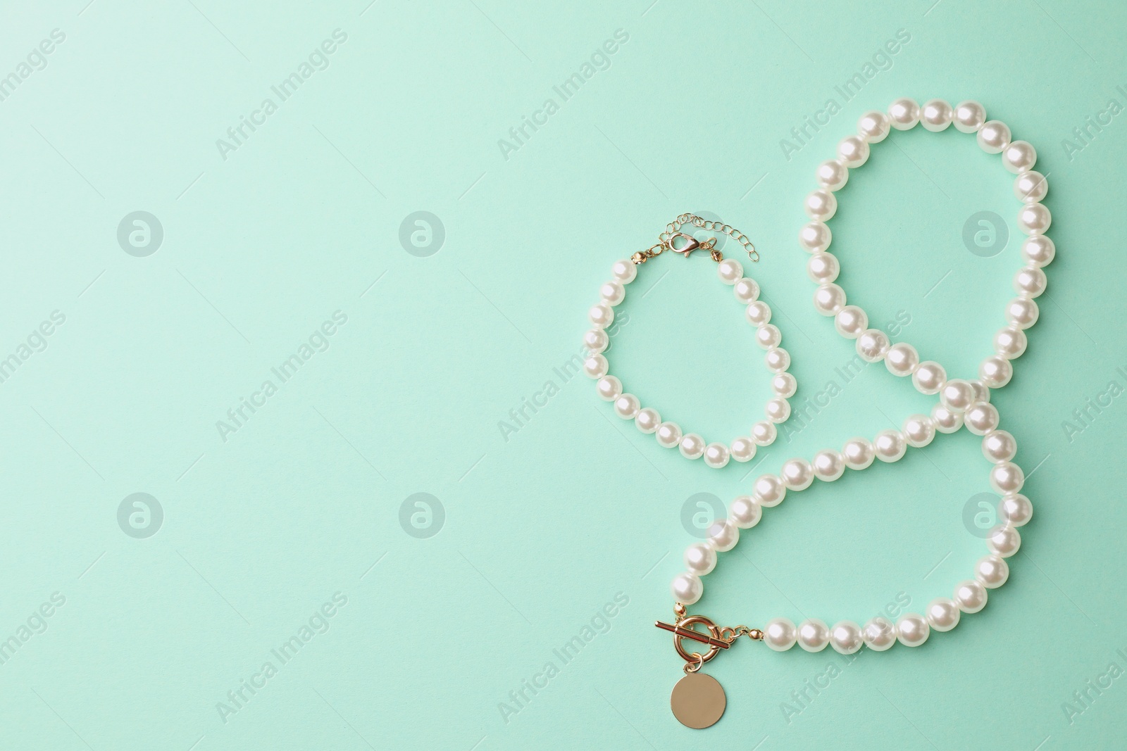 Photo of Elegant pearl necklace and bracelet on turquoise background, top view. Space for text