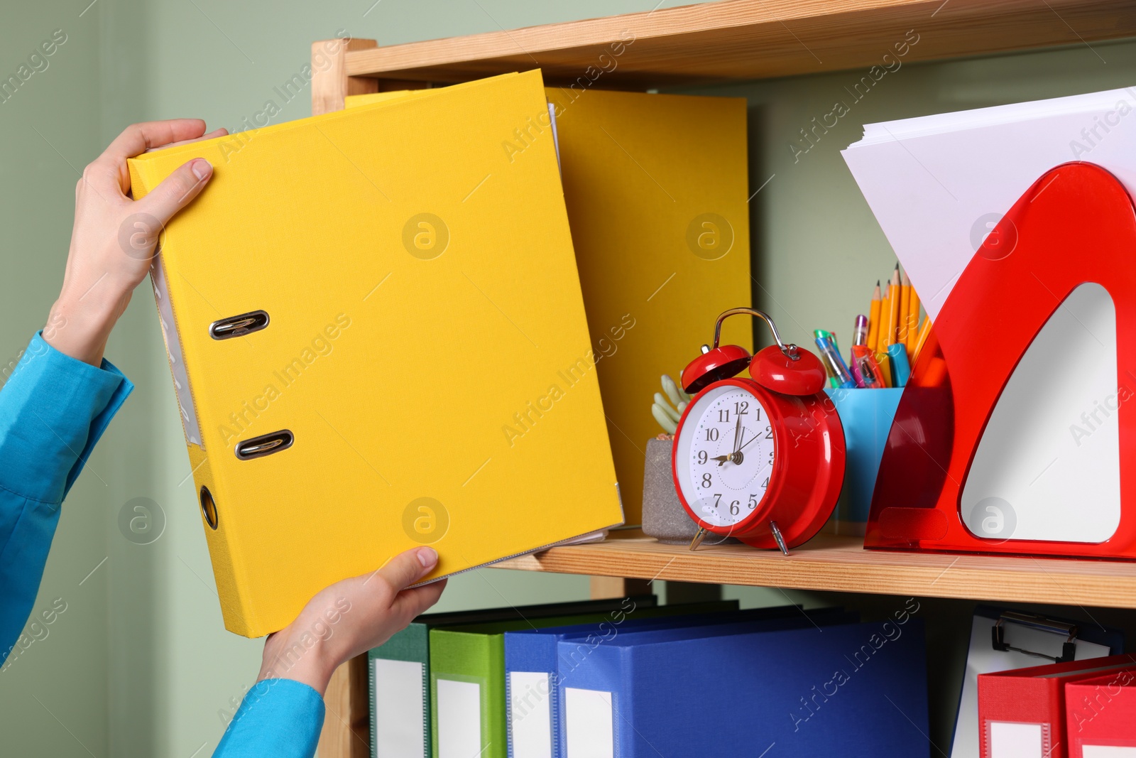 Photo of Woman taking binder office folder from shelving unit indoors, closeup