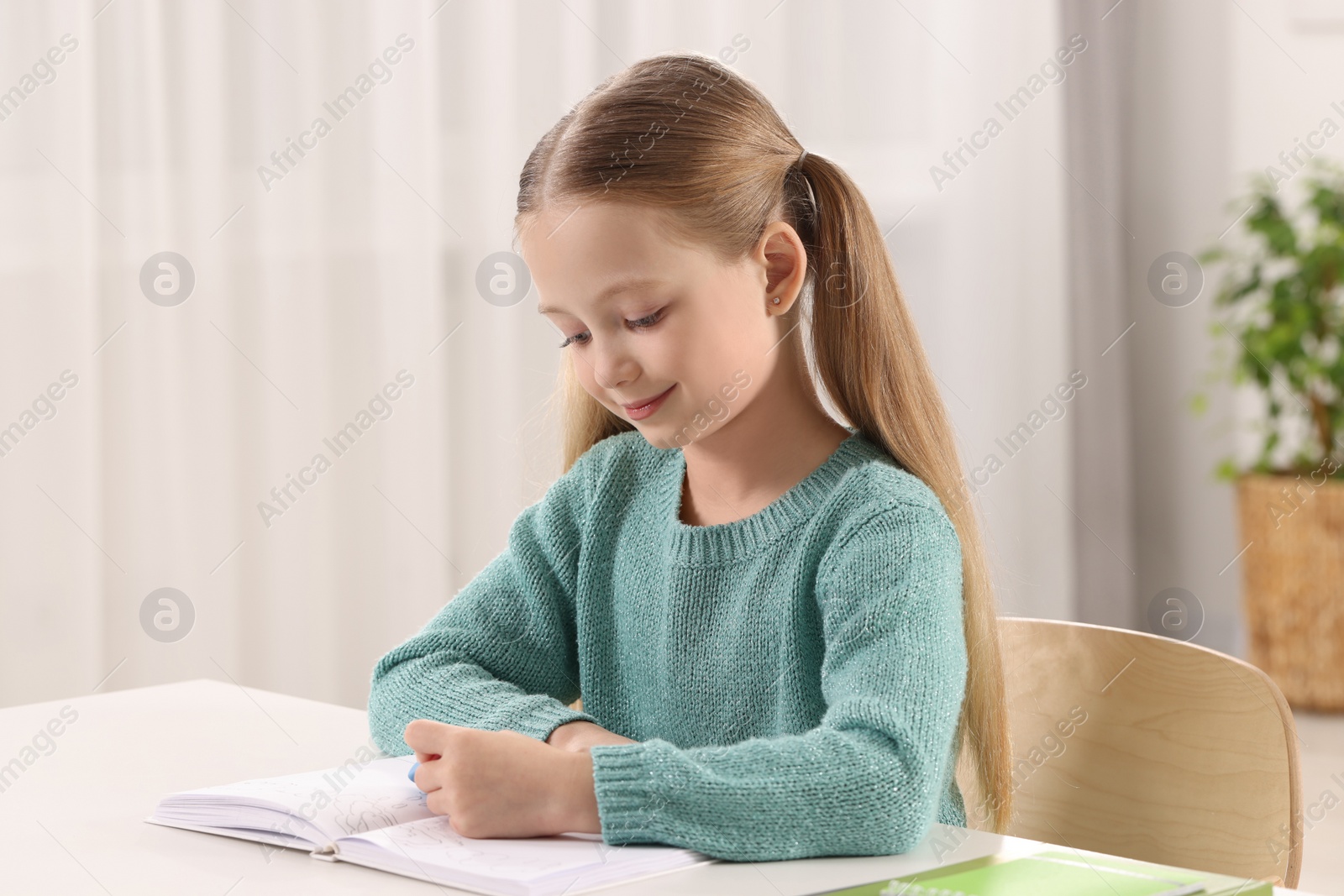 Photo of Girl using eraser at white desk in room