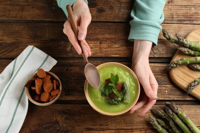 Photo of Woman with bowl of asparagus soup at wooden table, top view