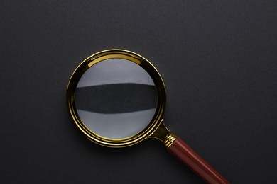 Photo of Magnifying glass on dark background, top view