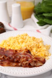 Delicious scrambled eggs with bacon in plate on white marble table