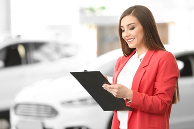 Photo of Young woman with clipboard in car salon