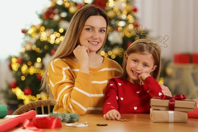Photo of Christmas presents wrapping. Happy mother and her little daughter at table with gift boxes in room