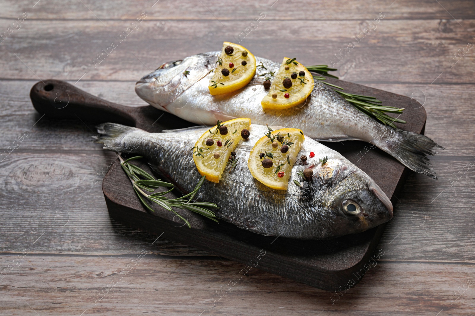 Photo of Fresh dorado fish, lemon slices and rosemary sprigs on wooden table