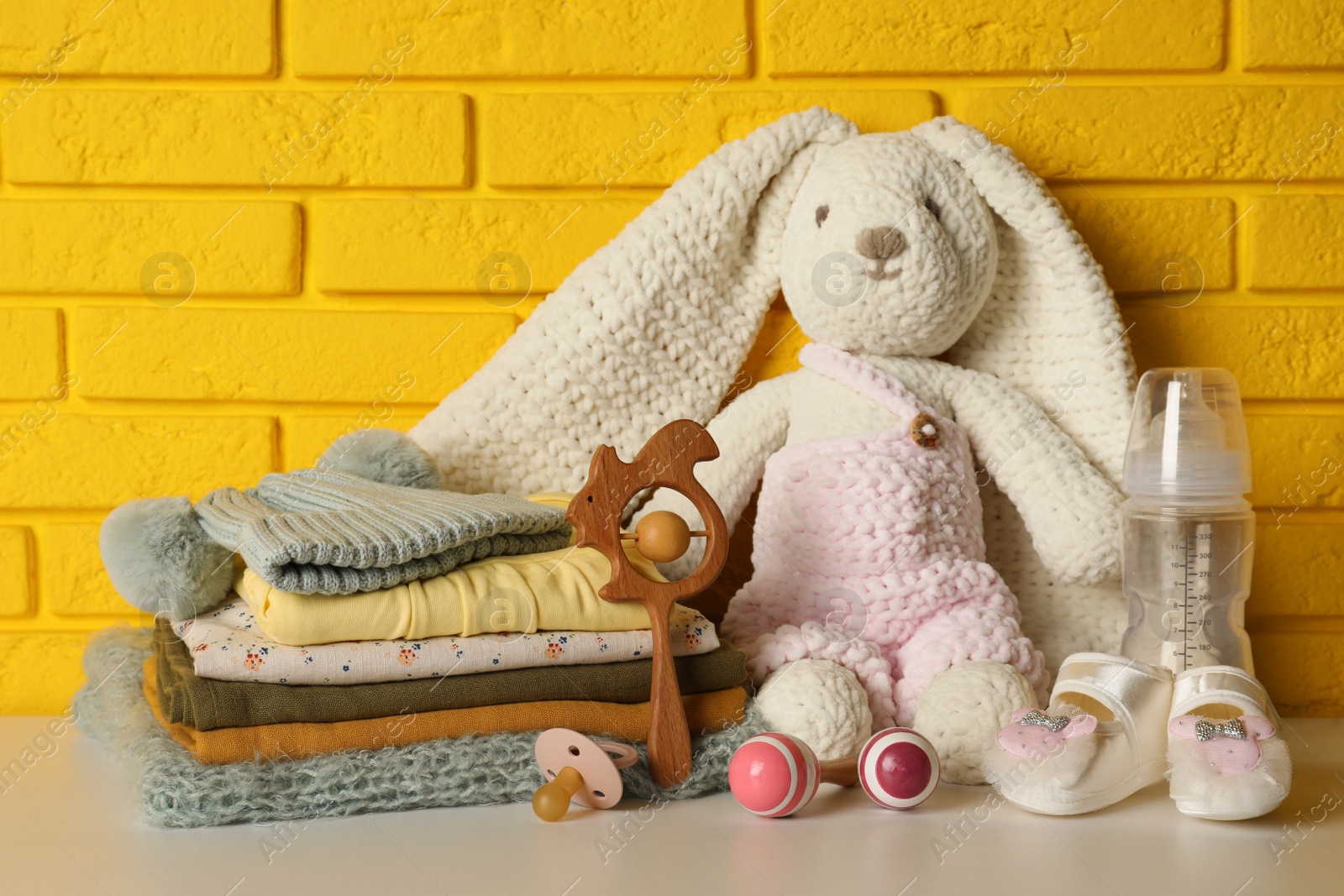 Photo of Baby clothes, toys and accessories on white table near yellow brick wall